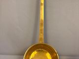 a brass spoon with a long handle on a white surface