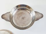 two silver dishes on a white table with a spoon and a bowl