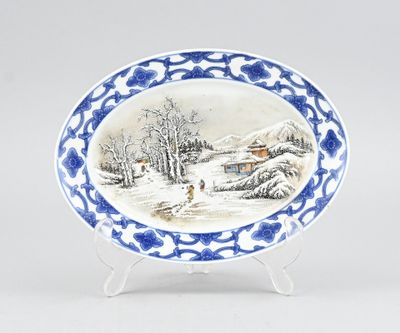 une assiette ovale bleue et blanche sur laquelle est représentée une scène hivernale