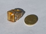 a gold ring with a citrine stone on it next to a coin