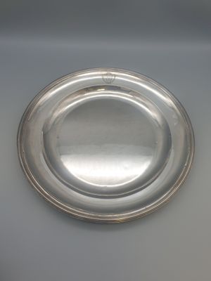 une plaque ovale en argent posée sur une surface blanche avec un fond noir