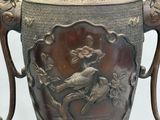 a large metal vase with a bird and flowers on it