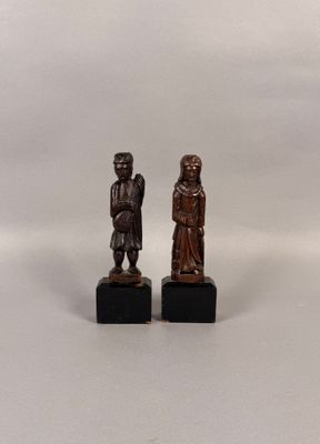 deux petites figurines en bois représentant un homme et une femme, posées sur des socles noirs