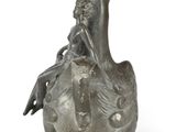 a silver vase with a bird on it on a white surface