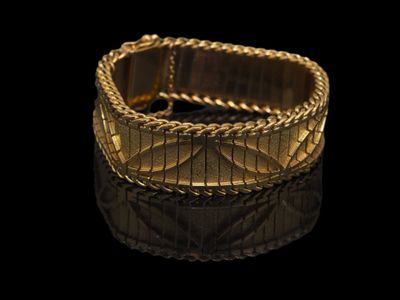 gros plan d'un bracelet en or sur une surface noire
