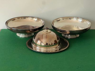 trois plats en métal plaqué argent posés sur une table verte recouverte d'une nappe verte