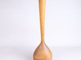 un vase orange muni d'une poignée en bois, posé sur une surface blanche