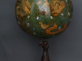 un globe vert et doré posé sur un socle en bois