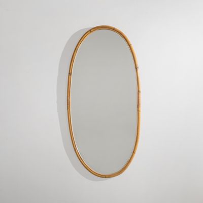 un grand miroir ovale avec un cadre en bambou accroché au mur
