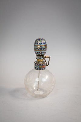 une petite bouteille en verre munie d'une poignée en métal, posée sur une surface blanche