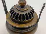 a small metal teapot with a handle on a white surface