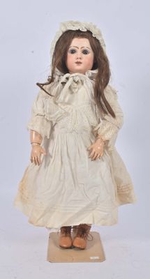 an antique doll with a white dress and bonnet on a wooden stand