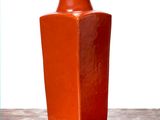 un vase orange posé sur une table, sur fond blanc
