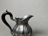 an antique silver pitcher with a curved handle on a gray surface