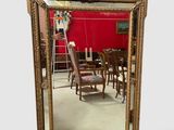 une image représentant un miroir avec un cadre doré et un mur rouge en arrière-plan