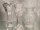 trois vases en verre posés sur une étagère en verre à côté d'une horloge