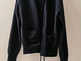 un cardigan noir suspendu à un cintre devant un mur blanc