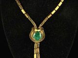 a gold necklace with a green stone pendant on a black mannequin
