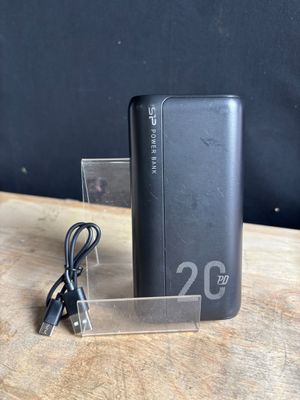 une batterie externe noire posée sur une table, à laquelle est branché un chargeur