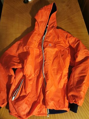 an orange jacket sitting on top of a wooden table next to a laptop computer