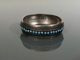 bague ornée de perles argentées et turquoise posée sur une surface réfléchissante