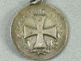 silver medal with a cross and laurels on it on a white surface