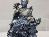 une statue représentant une femme assise sur un rocher, un oiseau dans la main