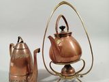 a small copper tea pot and a tea kettle on a stand