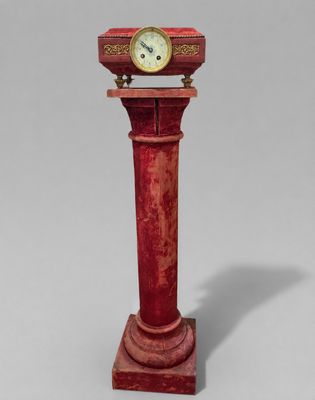 une horloge rouge posée sur un socle, sur fond gris