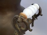 a bronze vase with a white bead on the handle