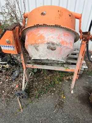 une bétonnière de couleur orange posée sur une palette à côté d'un bâtiment