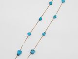 un long collier composé de perles de turquoise et d'une chaîne en or