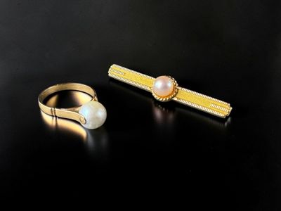 two gold rings and a pearl ring on a black surface