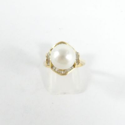 une photo d'une bague en perle blanche et diamants posée sur une surface blanche
