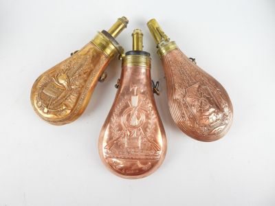 trois bouteilles en verre de couleur cuivrée, munies d'une poignée métallique, posées sur une surface blanche