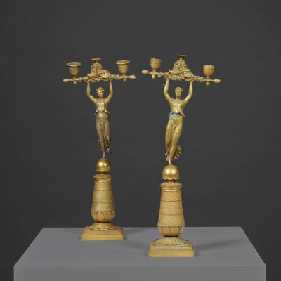 a pair of bronze figurines of women holding baskets on top of a pedestal