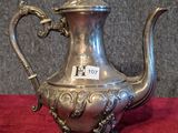 an antique silver tea pot with a handle on a red table cloth