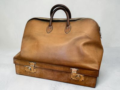 une valise en cuir marron posée sur une surface blanche, munie d'une poignée marron