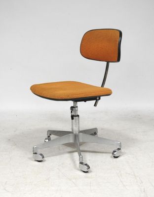 une chaise de bureau orange posée sur un sol blanc