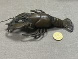 un petit homard en bronze posé sur une table, à côté d'une pièce de monnaie