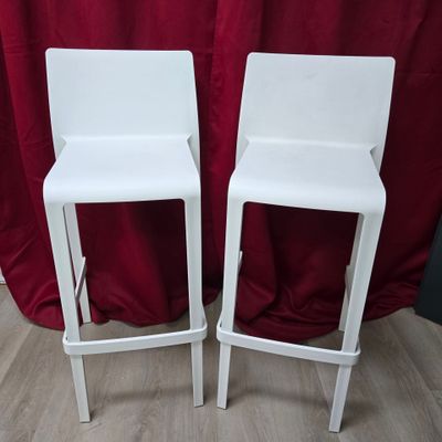 une paire de tabourets de bar blancs posés sur un sol en bois, devant un rideau rouge