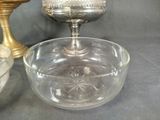 a glass bowl with a silver lid sitting next to a gold cup