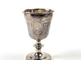 une coupe ancienne en argent posée sur une surface blanche, avec un fond blanc