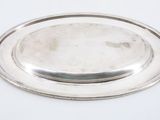 an oval silver plate with a raised edge on a white surface