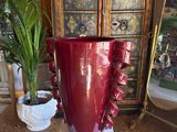 a large red vase sitting on a pedestal next to a potted plant