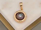 an image of a gold pendant with a black pearl on a marble surface