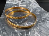 two gold bracelets sitting on a piece of plastic