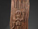 a carved plaque depicting a skeleton holding a human head