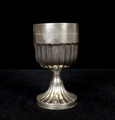 une coupe en argent posée sur une surface noire, sur fond noir