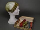 une tête de mannequin blanche coiffée d'un chapeau vert et accompagnée d'une boîte de cravates